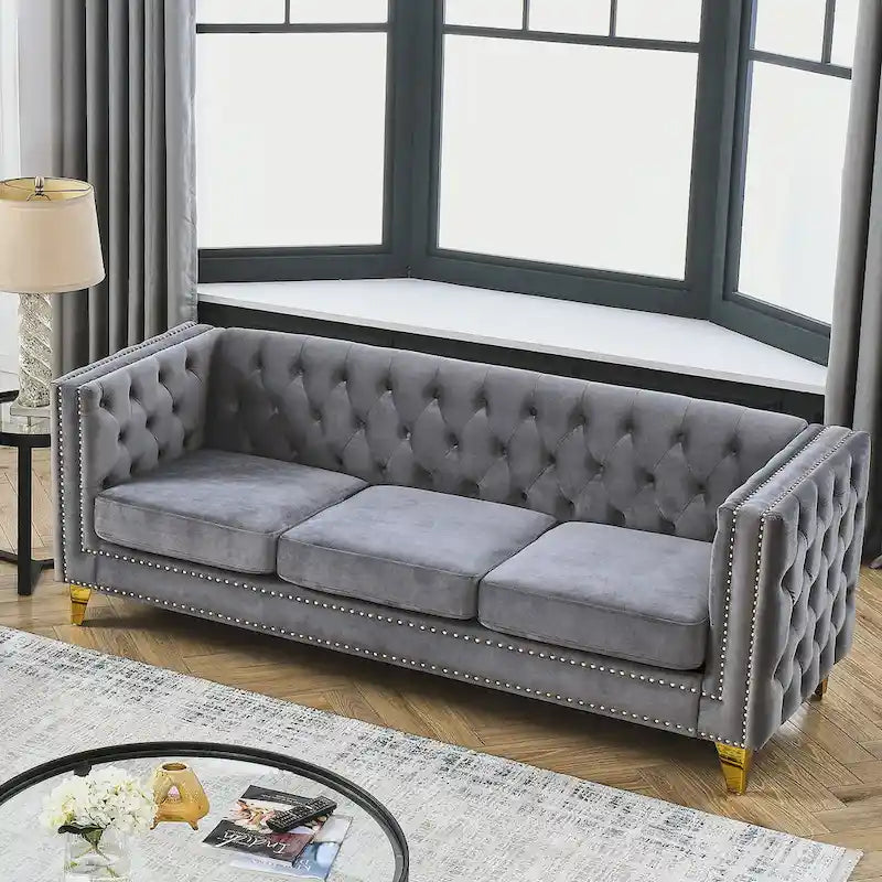 Sofá gris de terciopelo para tres personas, acolchado con botones decorativos, ribete de tachuelas y patas de metal